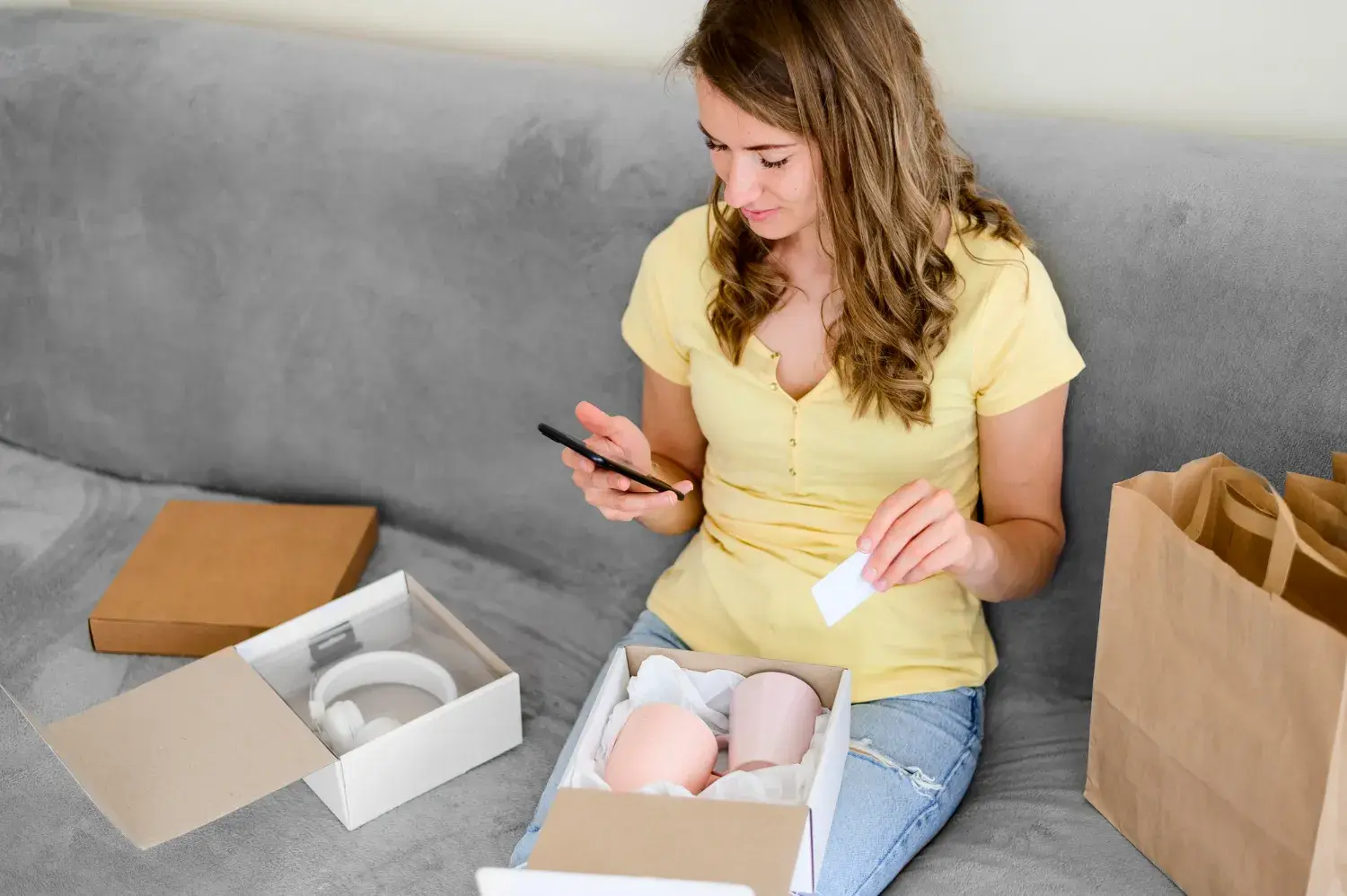 A woman packing items into boxes and looking at her cell phone while holding a label